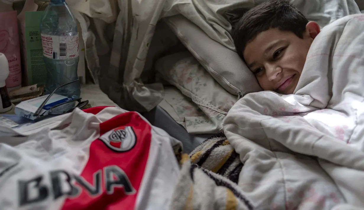 Daniel Dorado beristirahat di dekat jersey River Plate di rumahnya di daerah kumuh Costa Eperanza, Buenos Aires, 12 September 2020. Karena pandemi, Daniel yang bercita-cita menjadi pesepak bola di klub River Plate kini berlatih di rumah dengan instruksi dari pelatihnya. (ARIEL TIMY TORRES/AFP)