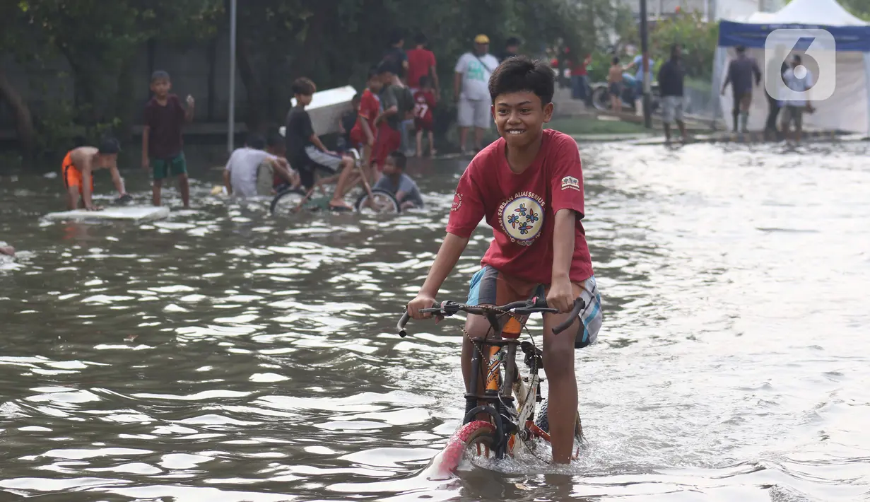 Seorang anak bermain sepeda di genangan air akibat banjir rob di kawasan pintu masuk Pelabuhan Nizam Zachman, Muara Baru, Jakarta, Jumat (5/6/2020). Banjir rob di Pelabuhan Muara Baru tersebut terjadi akibat cuaca ekstrem serta pasang air laut. (Liputan6.com/Helmi Fithriansyah)