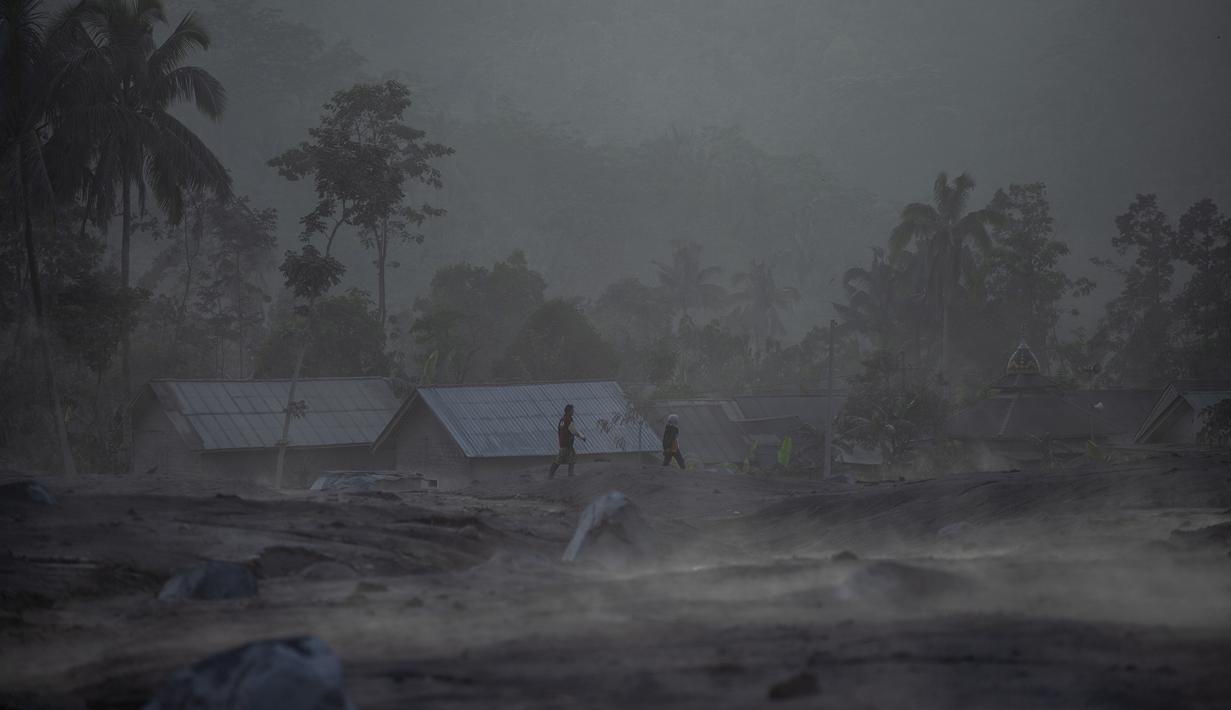 Orang-orang berjalan melewati rumah-rumah menyusul letusan gunung berapi oleh Gunung Semeru di desa Kajar Kuning di Lumajang (5/12/2022). Gunung Semeru meletus pada tanggal 4 Desember memuntahkan awan abu panas setinggi satu mil dan sungai lava di sisinya sambil memicu evakuasi hampir 2.000 orang tepat satu tahun setelah letusan besar terakhirnya menewaskan puluhan orang. (AFP/Juni Kriswanto)