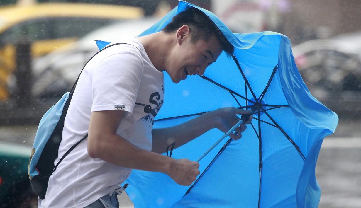 Seorang pria memegang payung sambil berjalan menghindari angin kencang yang disebabkan topan Dujuan di Taipei, Taiwan, Senin (28/9). Ribuan orang diungsikan untuk menghadapi topan Dujuan yang diprediksikan akan menyerang Taiwan. (REUTERS/Pichi Chuang)