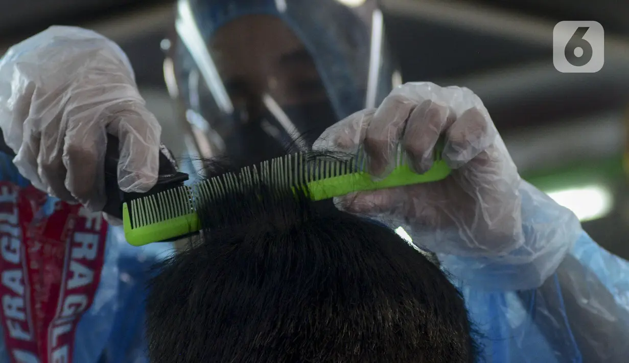 Tukang cukur mengenakan alat pelindung diri (APD) dari plastik saat mencukur rambut pelanggan di Pondok Kelapa, Jakarta, Selasa (5/5/2020). Tukang cukur mengenakan APD untuk mengurangi risiko penularan virus corona COVID-19. (merdeka.com/Imam Buhori)