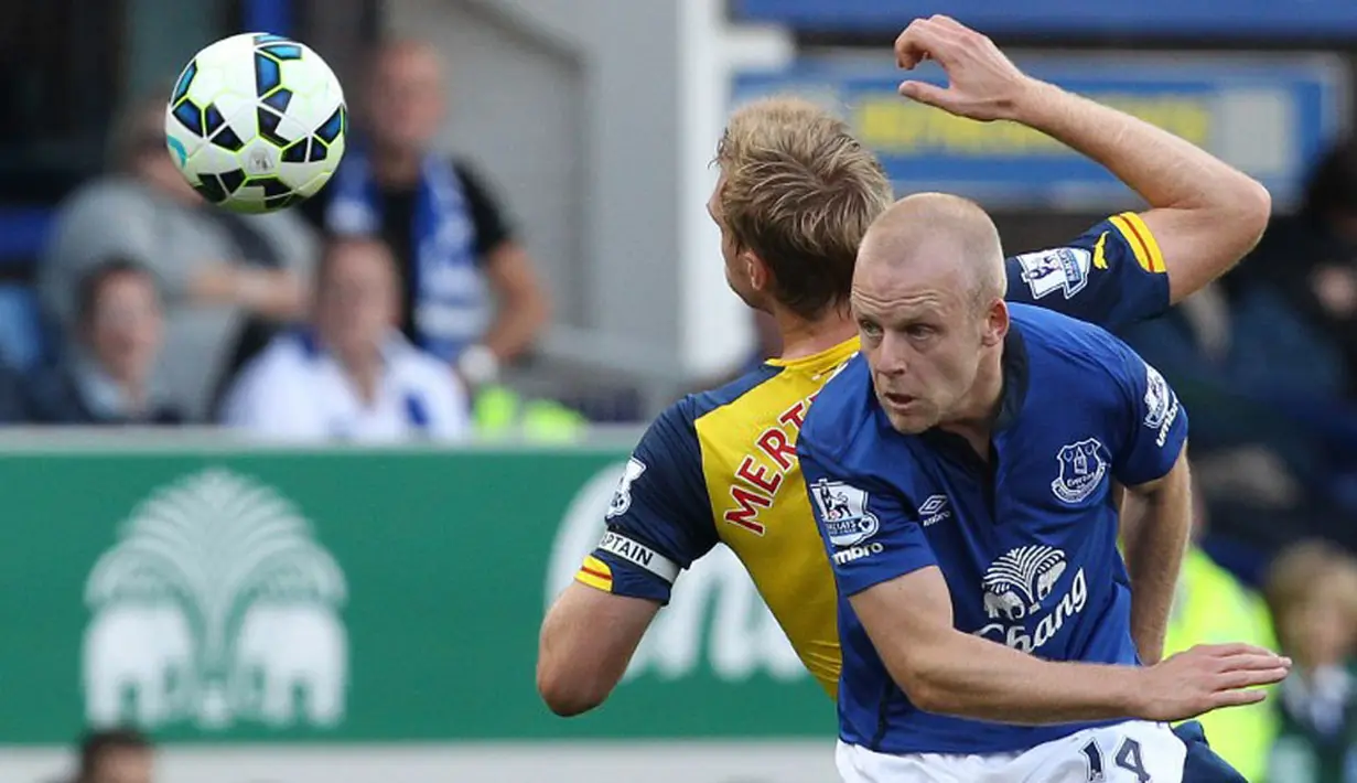 Pemain belakang Arsenal, Per Mertesacker (kiri) berjibaku berebut bola dengan penyerang Everton, Steven Naismith, dalam laga lanjutan Liga Primer Inggris di Stadion Goodison Park, (24/8/2014). (AFP PHOTO/Lindsey Parnaby)