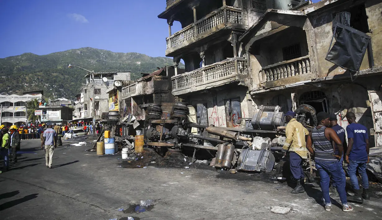 Petugas pemadam kebakaran berdiri dekat bangkai truk pengangkut BBM yang terbalik dan meledak di Cap-Haitien, Haiti, 14 Desember 2021. Ledakan tersebut menghanguskan mobil dan rumah serta menewaskan puluhan orang. (AP Photo/Joseph Odelyn)