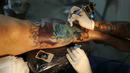 Seorang seniman terlihat serius menato seorang wanita dibagian kakinya saat Festival Internasional Tattoo Week Rio 2016 ketiga di Rio de Janeiro, Brasil, (22/1/2016). (REUTERS/Pilar Olivares)