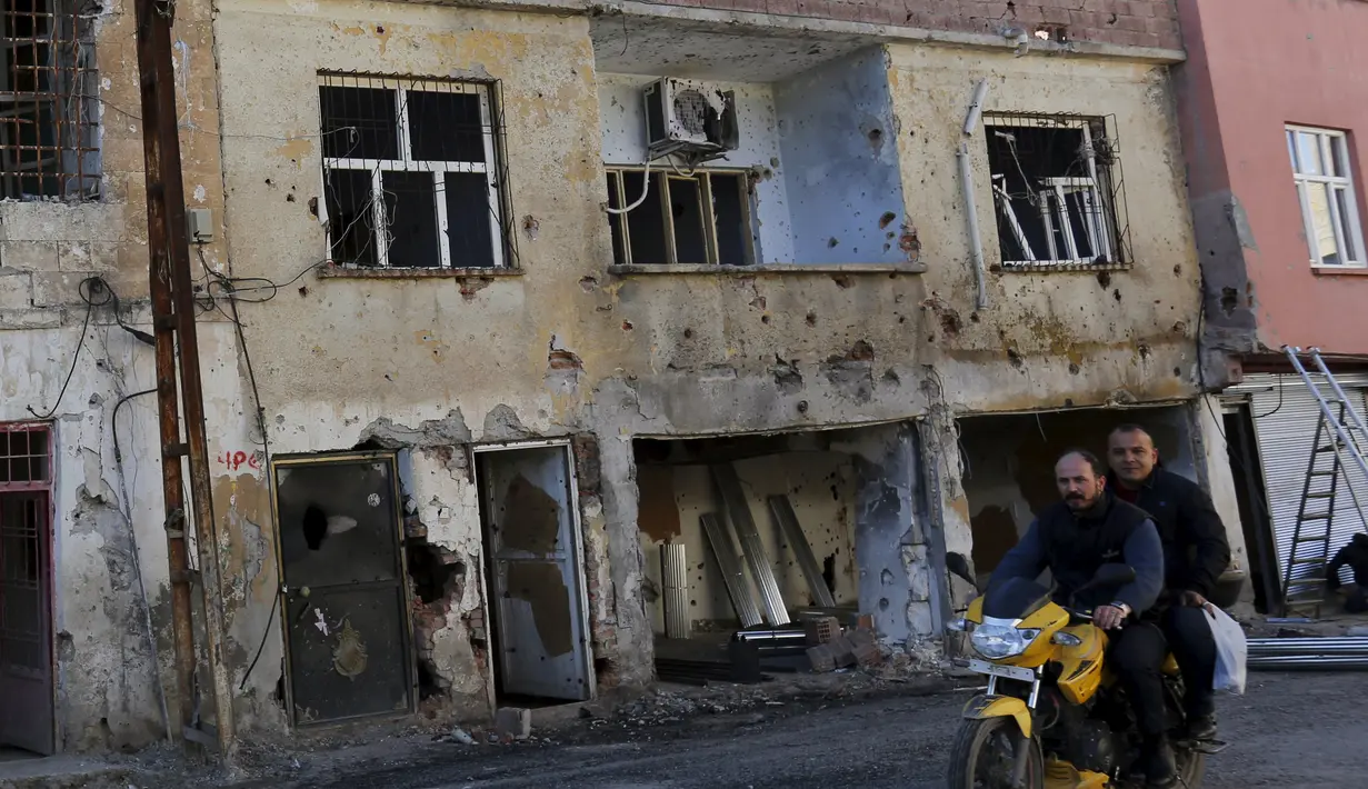  Warga melewati bangunan yang rusak akibat konflik antara Militer Turki dan Militan Kurdi di Turki, (7/12). Militan Kurdi dan afiliasinya Partai Pekerja Kurdi (PKK) dilabeli oleh pemerintah Ankara sebagai kelompok teroris. (REUTERS/Murad Sezer)