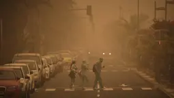 Sejumlah orang menyeberangi jalan saat badai pasir Gurun Sahara menerjang Santa Cruz de Tenerife, Kepulauan Canary, Spanyol, Minggu (23/2/2020). Pemerintah setempat menyarankan penduduk untuk tetap di dalam rumah. (AP Photo/Andres Gutierrez)