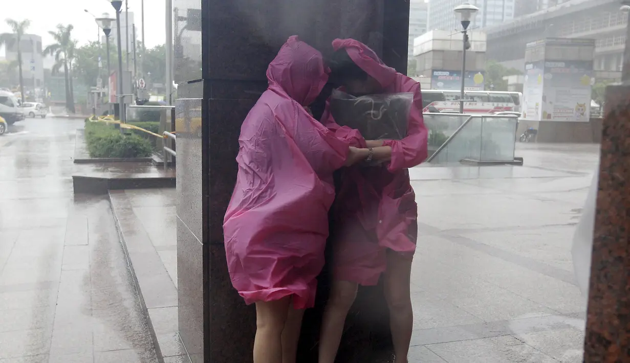 Dua wanita berlindung di dinding untuk menghindari angin kencang yang disebabkan topan Dujuan di Taipei, Taiwan, Senin (28/9). Ribuan orang diungsikan untuk menghadapi topan raksasa Dujuan yang diprediksikan akan menyerang Taiwan.(REUTERS/Pichi Chuang)