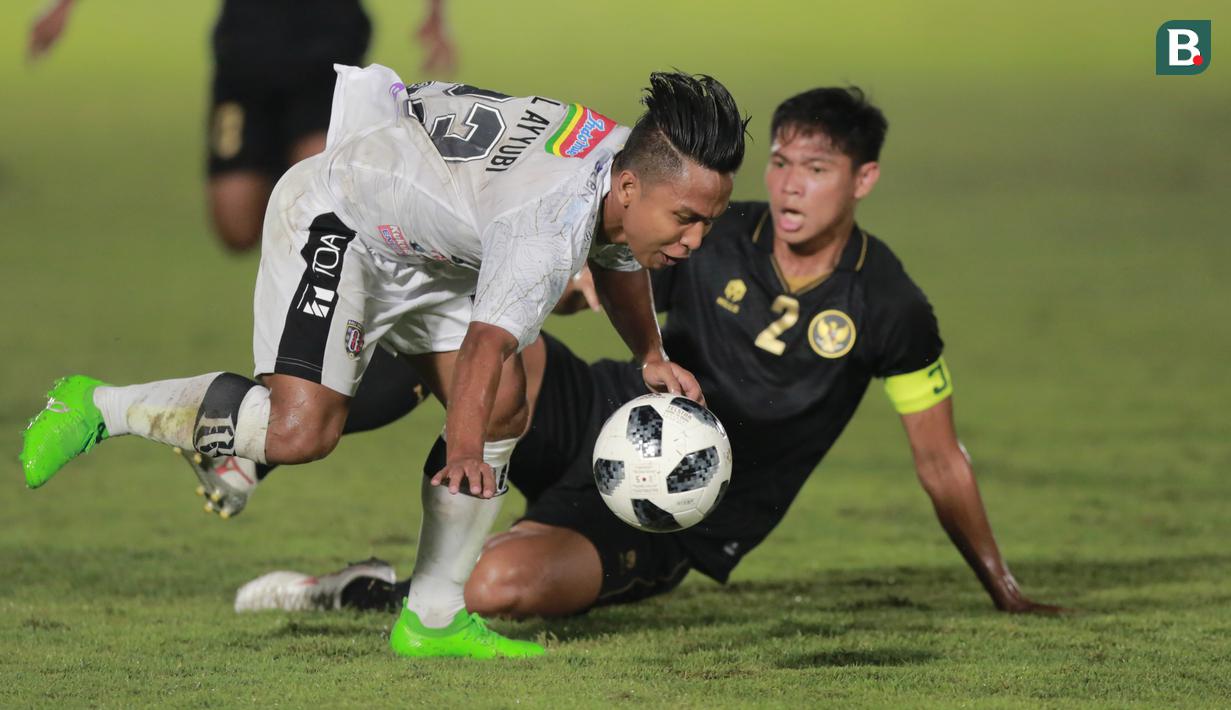 Pemain Bali United, Fahmi Al-Ayyubi, terjatuh saat berebut bola dengan bek Timnas Indonesia, Andy Setyo, pada laga uji coba di Stadion Madya, Minggu (7/3/2021). (Bola.com/ Ikhwan Yanuar Harun)