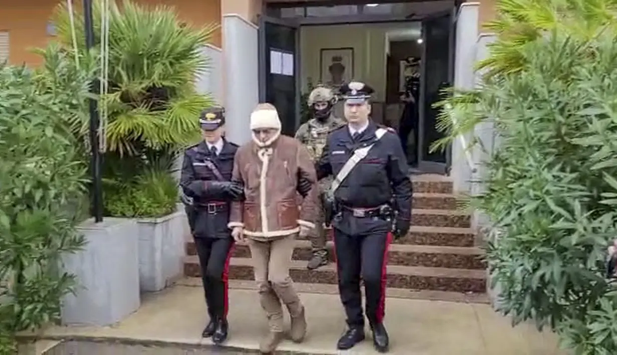 Dalam gambar yang diambil dari video pada Senin, 16 Januari 2023 menunjukkan bos mafia paling dicari Matteo Messina Denaro meninggalkan barak Carabinieri Italia segera setelah penangkapannya di sebuah klinik swasta di Palermo, Sisilia. Sepasang petugas Carabinieri, masing-masing memiting tangan Matteo Messina, mengantarnya menuruni tangga depan klinik dan membawanya ke sebuah van hitam. (Carabinieri via AP)