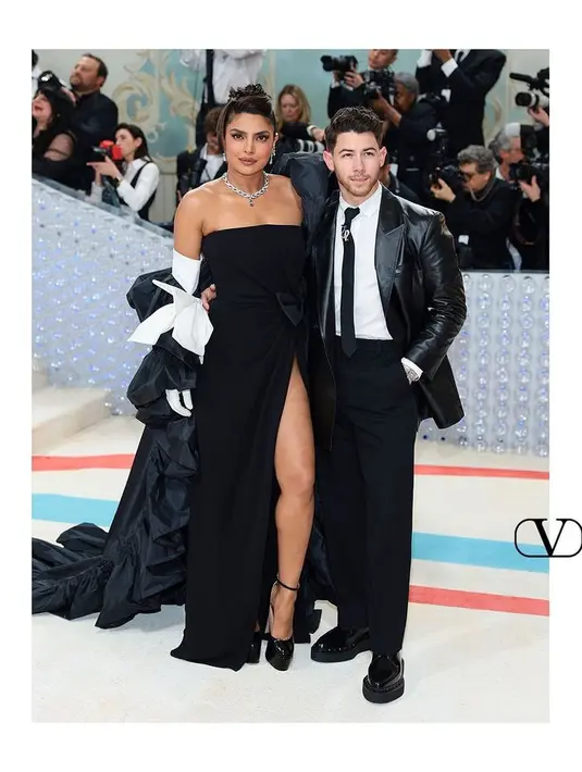 Ratu kecantikan berdarah India Priyanka Chopra tampil dengan strapless dress hitam. Dengan detail pita putih pada gloves leather ditambah cape yang menjuntai ke lantai. [Foto: @maisonvalentino]