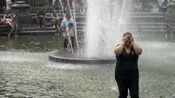 Seorang wanita cuci muka di air mancur saat siang hari yang panas di Washington Square Park di New York City (17/7/2019). Panas terik bergerak ke daerah Kota New York, dengan suhu yang diperkirakan akan mencapai 100 derajat pada akhir pekan ini. (AFP Photo/Drew Angerer)