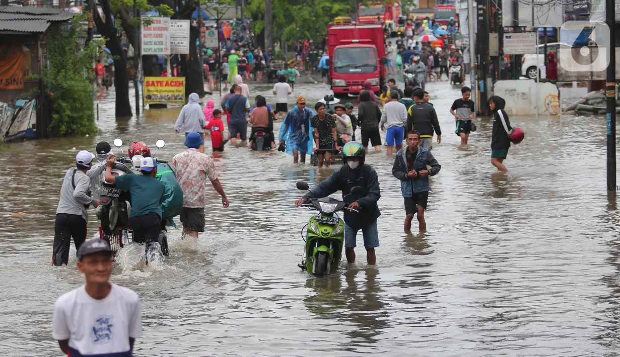 Warga berusaha melintasi genangan air ketika banjir merendam Jalan KH. Hasyim Ashari, Tangerang, Banten, Sabtu (16/7/2022). Akibat luapan kali angke ruas jalan yang menghubungkan Tangerang-Jakarta itu terputus akibat banjir. (Liputan6.com/Angga Yuniar)