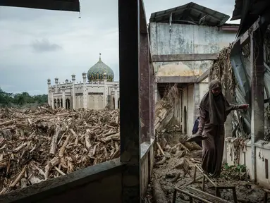 Seorang siswi berjalan di atas bangku untuk menghindari lumpur karena tumpukan pohon tumbang yang tersapu banjir bandang masih berada di Pesantren Darul Mukhlisin dan masjid yang terhubung dengannya di Aceh Tamiang, pada Minggu 14 Desember 2025. Pemandangan memprihatinkan masih terlihat di Pondok Pesantren Darul Mukhlisin, Aceh Tamiang, Minggu (14/12/2025). (Yasuyoshi Chiba/AFP)