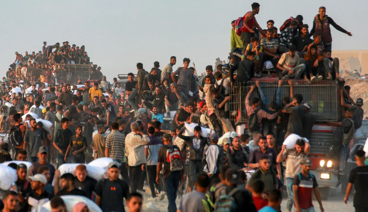 Orang-orang naik ke atas dan bergelantungan di atas truk yang mengangkut mereka, sementara yang lain berjalan sambil membawa karung-karung tepung di sepanjang jalan al-Rashid di Jabalia Barat pada 17 Juni 2025. (BASHAR TALEB/AFP)