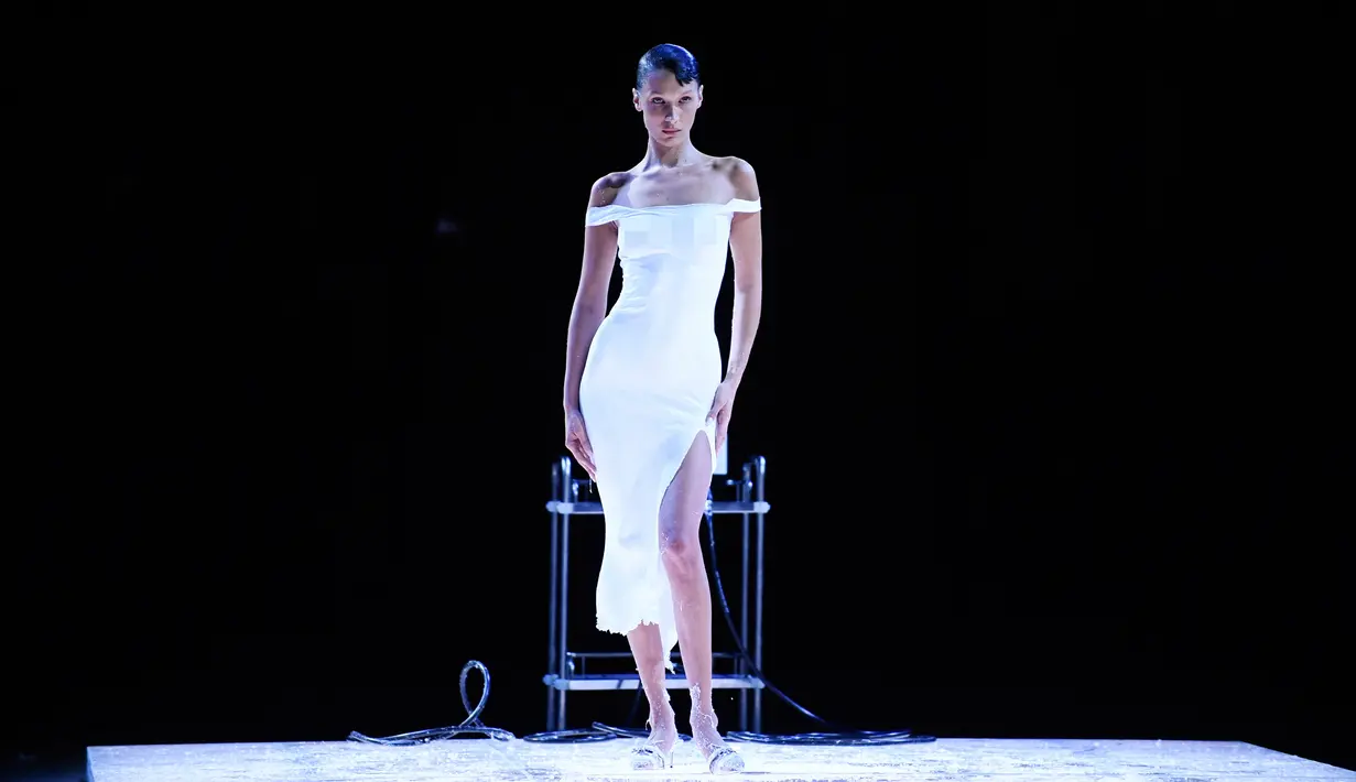 <p>Model AS Bella Hadid berbusana dengan cairan yang disemprotkan ke tubuhnya saat peragaan busana Coperni Spring-Summer 2023 pada Paris Fashion Week di Paris, Prancis, 30 September 2022. Beberapa menit setelah sedikit penyesuaian, Bella Hadid melenggang di runway dengan balutan dress putih yang nampak pas membentuk lekuk tubuhnya. (JULIEN DE ROSA/AFP)</p>
