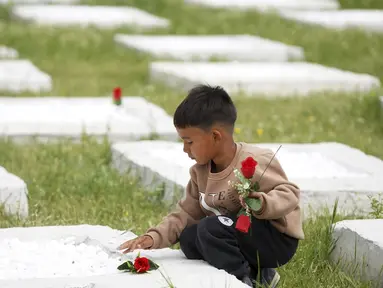 Seorang anak laki-laki meletakkan bunga di atas kuburan di pemakaman di desa Kato Tritos di pulau Lesbos, Laut Aegea timur laut, Yunani, Rabu (17/4/2024). (AP Photo/Panagiotis Balaskas)