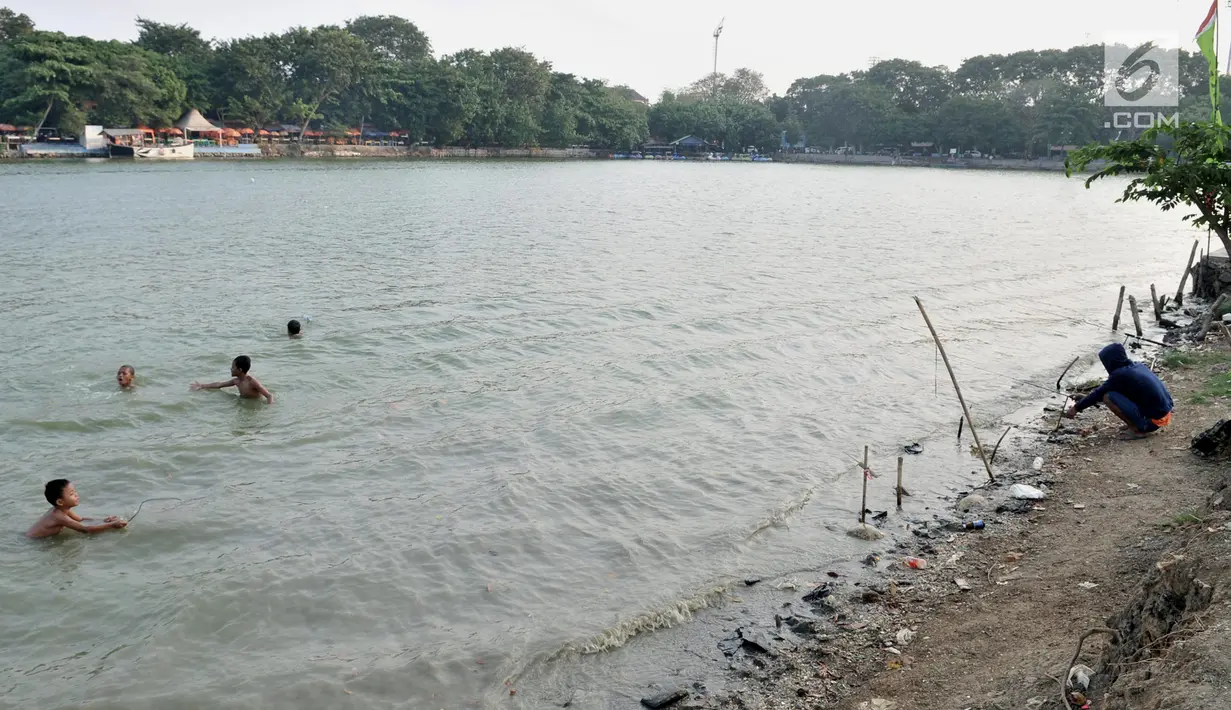 Anak-anak berenang dekat pemancing di Danau Sunter, Jakarta, Selasa (23/7/2019). Anak-anak tetap nekat berenang di Danau Sunter kendati mereka sadar telah dilarang dan dapat membahayakan diri sendiri. (merdeka.com/Iqbal Nugroho)
