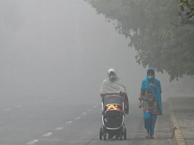 Seorang wanita berjalan di sepanjang jalan yang diselimuti kabut asap di Lahore pada Kamis 14 November 2024. (Arif ALI/AFP)