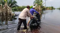 Personel Polres Pelalawan membantu dorong sepeda motor warga yang mogok karena nekat melintasi banjir di Jalan Lintas Timur Sumatra. (Liputan6.com/M Syukur)