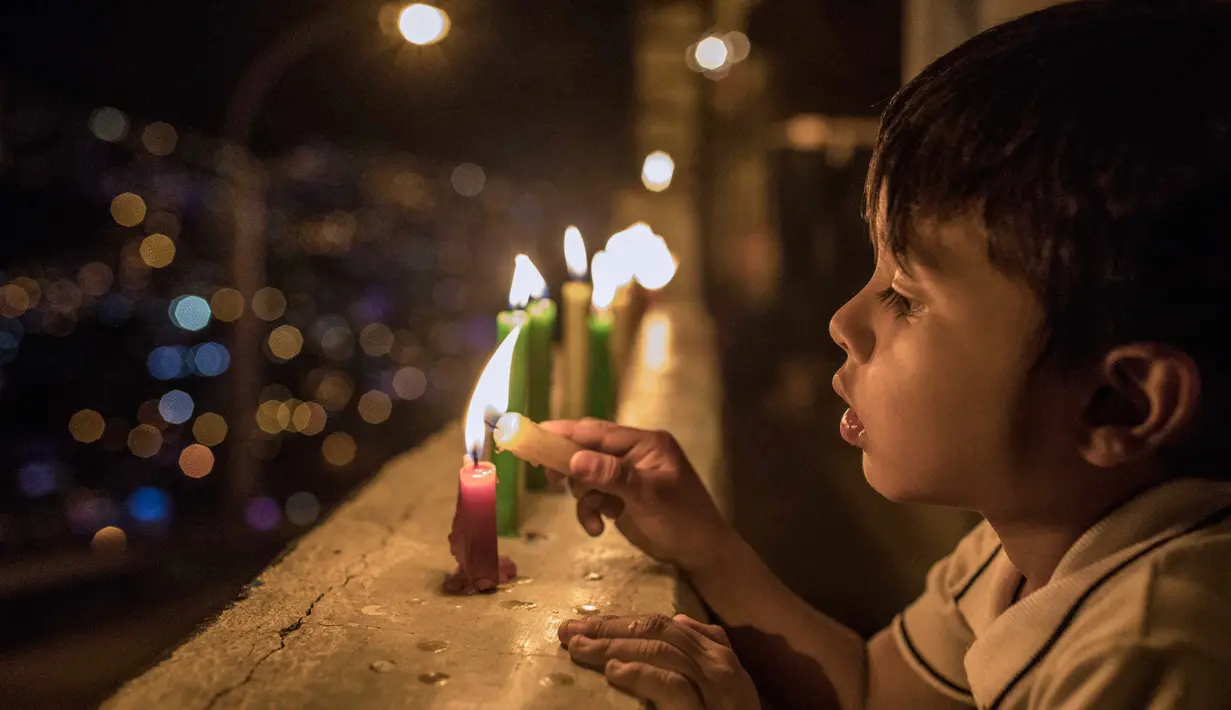 Seorang anak menyalakan lilin selama Hari Lilin Kecil di Medellin, Kolombia (7/12). Hari Lilin Kecil (bahasa Spanyol : Día de las Velitas) adalah salah satu dari hari raya tradisional yang paling dirayakan di Kolombia. (AFP Photo/Joaquin Sarmiento)