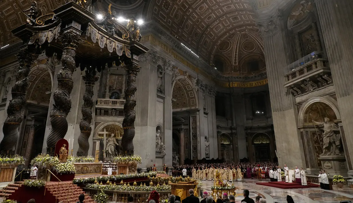 Ketika Misa Malam Natal berakhir, Paus, yang didorong dengan kursi roda, turun ke basilika dengan patung Bayi Yesus seukuran manusia di pangkuannya dan diapit oleh anak-anak yang membawa karangan bunga. Patung itu ditempatkan di palungan di kandang Natal di basilika. (AP Photo/Gregorio Borgia)