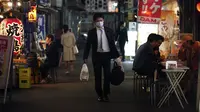 Seorang pria yang mengenakan masker berjalan mlewati bar jalanan di Tokyo, Jepang, 28 April 2020. Pandemi virus corona COVID-19 mengadu kelompok yang bersedia mengikuti peraturan tetap tinggal di rumah dengan mereka yang menolaknya. (AP Photo/Eugene Hoshiko, File)