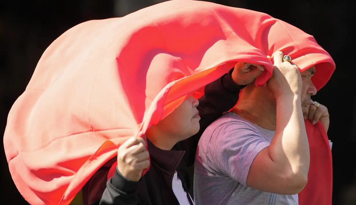Seorang pria dan perempuan menutupi kepala mereka dengan kain untuk melindungi mereka dari sinar matahari di Manila, Filipina, Senin (29/4/2024). (AP Photo/Aaron Favila)