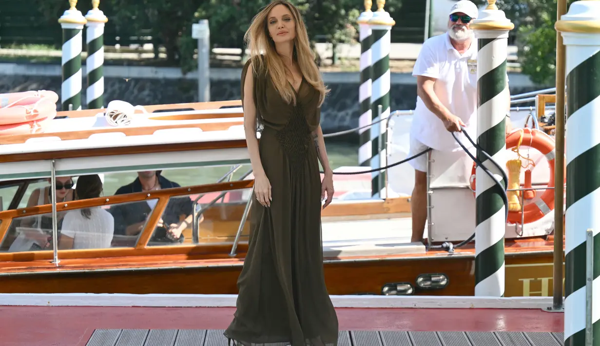 <p>Jolie pertama kali tiba di Venice dengan gaun V-neck coklat tipis dari Saint Laurent, yang dipasangkan dengan anting-anting berlian Jessica McCormack dan cincin yang serasi. (Alberto PIZZOLI / AFP)</p>