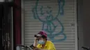 Seorang wanita melihat teleponnya di dekat grafiti yang menggambarkan seorang biarawan di Beijing (24/5/2022). Beijing memperpanjang perintah bagi pekerja dan pelajar untuk tinggal di rumah dan memerintahkan pengujian massal tambahan pada Senin ketika kasus COVID-19 meningkat di ibu kota China. (AP Photo/Ng Han Guan)