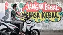 Pengendara motor melintasi mural bertema imbauan protokol kesehatan COVID-19 di kawasan Cakung Barat, Jakarta, Minggu (18/10/2020). Mural karya warga setempat tersebut bertujuan mengingatkan masyarakat akan pentingnya memakai masker, menjaga jarak, dan mencuci tangan. (merdeka.com/Iqbal S. Nugroho)