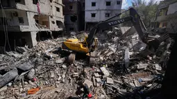 Data Kementerian Kesehatan Lebanon, per 4 April 2026, mencatat 1.368 warga sipil tewas dan 4.138 luka-luka akibat serangan udara Israel. Tampak dalam foto, sebuah ekskavator membersihkan puing-puing sementara seorang pria membawa barang-barang miliknya berjalan melewati reruntuhan di lokasi serangan Israel pada Minggu 5 April 2026 terhadap sebuah bangunan di lingkungan Jnah, Beirut, Lebanon, Senin 6 April 2026. (AP Photo/Hassan Ammar)