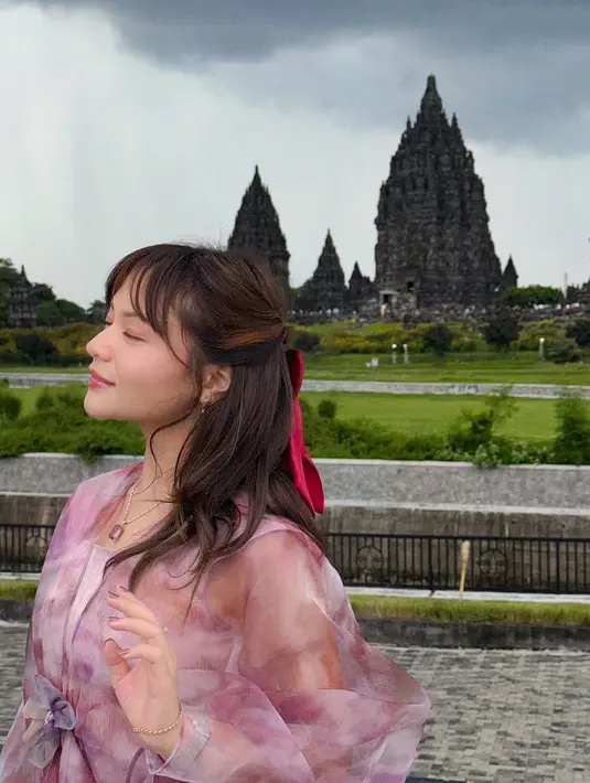 Serta, bagian luar berupa outer transparan berbahan organza atau sifon dengan warna gradasi ungu dan pink, yang mengalir lembut dan memberi siluet anggun. Outer dengan potongan longgar dan dihiasi aksen bunga di bagian pinggang sebagai pemanis. (Liputan6.com/IG/@amelcarla)