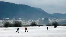 Dua orang pria bermain hoki es sambil berseluncur di atas sungai Doubs yang membeku di perbatasan Perancis Les Brenets, Swiss, Senin (2/1). Sungai ini menjadi objek wisata es yang diminati warga. (REUTERS/Denis Balibouse)