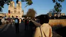 Orang-orang berhenti di depan Katedral Notre Dame yang kembali membunyikan lonceng utamanya di Paris, Rabu (15/4/2020). Lonceng utama katedral kembali dibunyikan setelah satu tahun mengalami kebakaran yang sampai mengejutkan seluruh warga dunia. (AP/Christophe Ena)