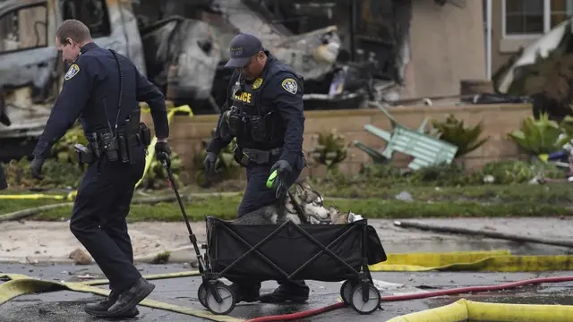 Polisi membantu menyelamatkan anjing-anjing dari sebuah rumah setelah pesawat jatuh di kawasan permukiman San Diego, AS, Kamis, 22 Mei 2025. (AP/Gregory Bull)