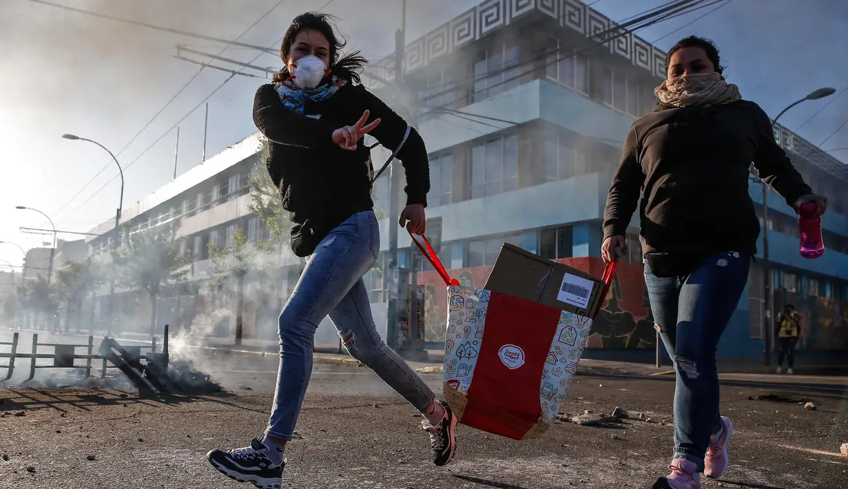 Penjarah melambaikan tanda 'V' ketika berlari selama protes di Valparaiso, Chile, Minggu (20/10/2019). Bentrokan pecah di Santiago setelah dua orang tewas ketika sebuah supermarket dibakar ketika protes terhadap kondisi ekonomi dan ketidaksetaraan sosial. (JAVIER TORRES/AFP)