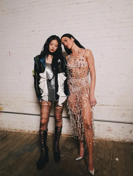 Jennie padukan minidress metalik dengan ripped stocking dan boots tinggi. Dipadu dengan jaket tartan berdetail ruffle putih [@dualipa]