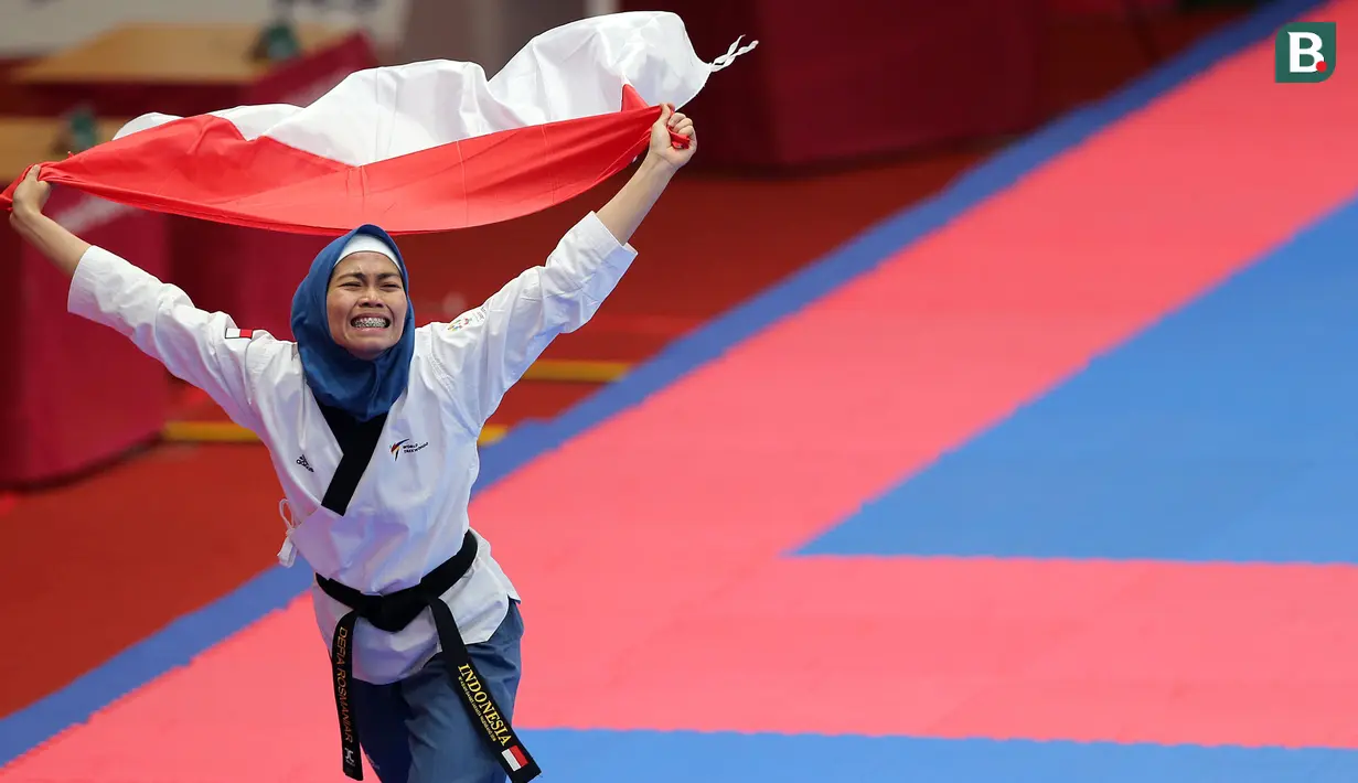 Atlet taekwondo, Defia Rosmaniar, melakukan selebrasi usai berhasil meriah medali emas pertama untuk Indoensia di Asian Games 2018 di JCC, Jakarta, Minggu (19/8/2018). (Bola.com/Peksi Cahyo)
