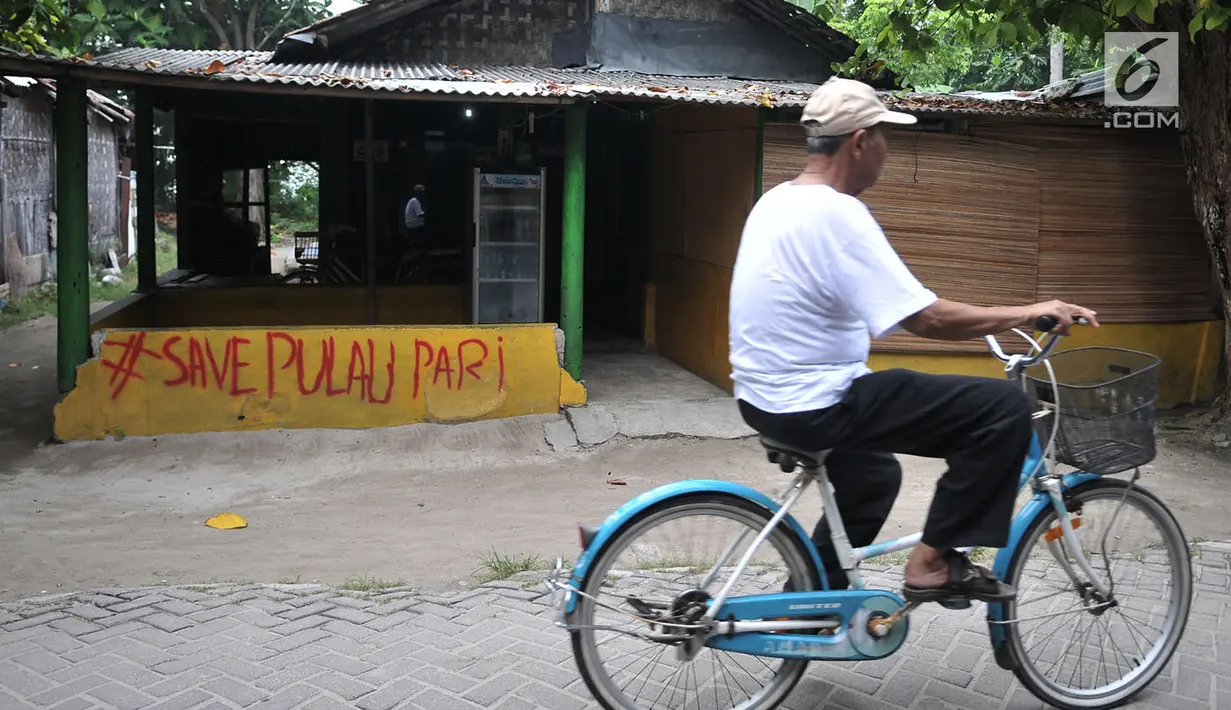 Wisatawan bersepeda melintasi coretan protes di salah satu tembok rumah di Pulau Pari, Kepulauan Seribu, Jakarta, Minggu (29/4). Coretan dibuat warga yang menolak klaim PT Bumi Pari Asri atas kepemilikan lahan Pulau Pari. (Merdeka.com/Iqbal S. Nugroho)