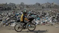 Anak-anak Palestina mengayuh sepeda melewati tempat pembuangan sampah besar di sepanjang jalan utama di Kota Gaza pada 24 Februari 2024. (Foto oleh AFP)