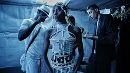 Desainer Oumar Dicko (kanan) dari Mali dan Belgia memakaikan busana kreasinya ke salah satu model  belakang panggung Dakar Fashion Week di ibukota Senegal, (1/7). (AP Photo / Finbarr O'Reilly)