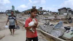 Akses jalan hingga tumpukan material banjir masih menyulitkan relawan untuk segera melakukan evakuasi korban. Tampak dalam foto, seorang penyintas menggendong kucing sambil berjalan di area yang terdampak banjir bandang di Aceh Tamiang, Pulau Sumatra, Jumat 5 Desember 2025. (AP Photo/Binsar Bakkara)