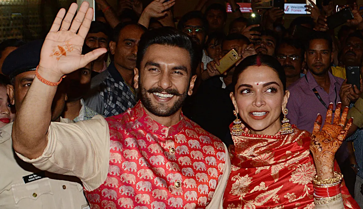 Pasangan pengantin baru, Ranveer Singh dan Deepika Padukone menyapa penggemar yang menyambut mereka di bandara internasional Mumbai, Minggu (18/11). Pasangan bintang Bollywood India itu baru saja kembali dari acara pernikahan mereka di Italia. (AFP)