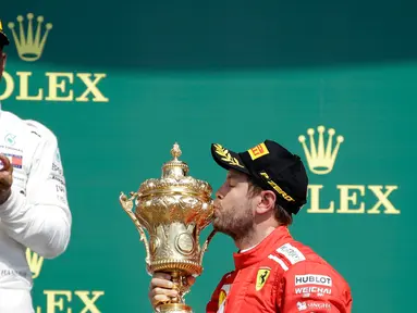 Pembalap Ferrari, Sebastian Vettel (benar) mencium piala di depan pembalap Mercedes, Lewis Hamilton (kiri) saat menjuarai F1 GP di Sirkuit Silverstone, Inggris, Minggu (8/7). Vettel mengungguli Lewis Hamilton dan Kimi Raikkonen. (AP Foto/Luca Bruno)