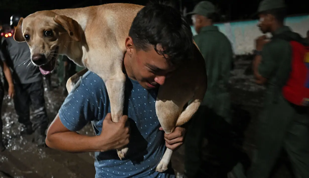 Seorang pria membawa anjingnya setelah tanah longsor akibat hujan lebat di El Castaño, Venezuela, Senin (17/10/2022). Petugas penyelamat terus berupaya membersihkan gundukan puing-puing di kota Las Tejerías yang dilanda bencana tanah longsor.  (Federico Parra / AFP)