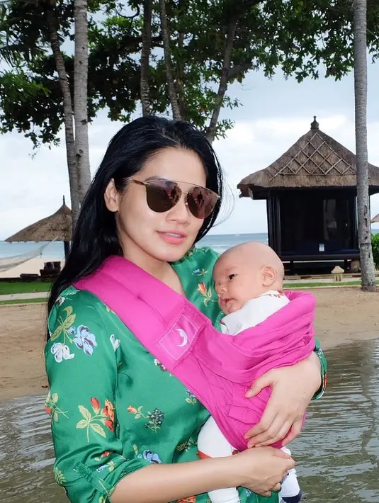 Sama halnya dengan yang satu ini, Titi tetap kece memakai baju hijau dan kacamata hitsnya sambil menggendong Kai menggunakan gendongan berwarna pink. Mesra banget ya ibu dan anak ini? (Instagram/titi_kamall)