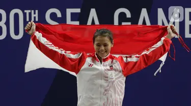 Lifter Windy Aisyah mengibarkan bendera saat naik podium usai mendapatkan medali emas SEA Games 2019 cabang angkat besi nomor 49 kg di Stadion Rizal Memorial, Manila, Minggu (1/12/2019). Windy Aisyah meraih emas dengan total angkatan 104 kg. (Bola.com/M Iqbal Ichsan)