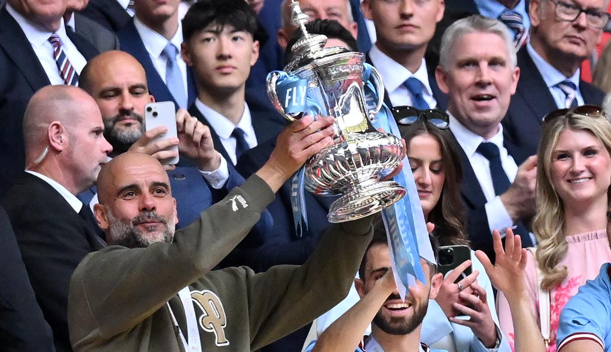 Selebrasi pelatih Manchester City, Pep Guardiola dengan trofi Piala FA 2022/2023 setelah mengalahkan Manchester United 2-1 pada laga final di Wembley Stadium, London (3/6/2023). (AFP/Glyn Kirk)