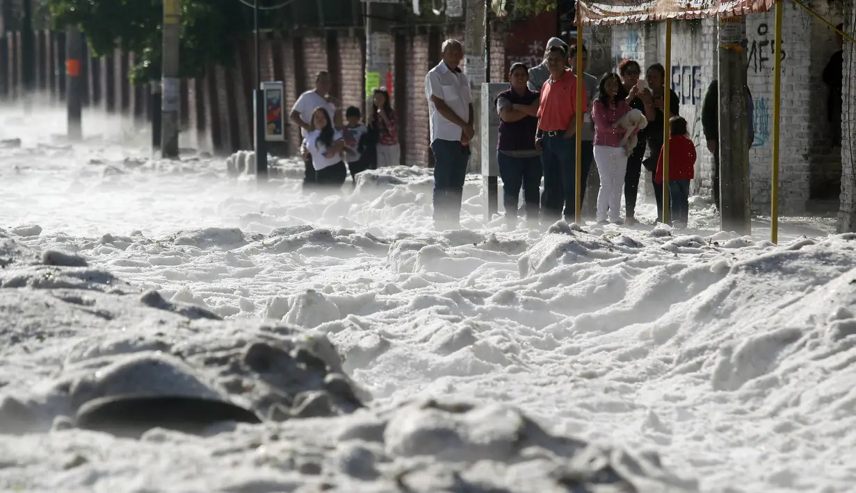 Sejumlah warga berdiri di trotoar melihat salju tebal yang menutupi jalan di wilayah timur Guadalajara, Jalisco, Meksiko (30/6/2019). Pemerintah daerah setempat mengatakan sebanyak 200 rumah rusak dan puluhan kendaraan tersapu di dalam kota dan beberapa distrik di sekitarnya. (AFP Photo/Ulises Ruiz)