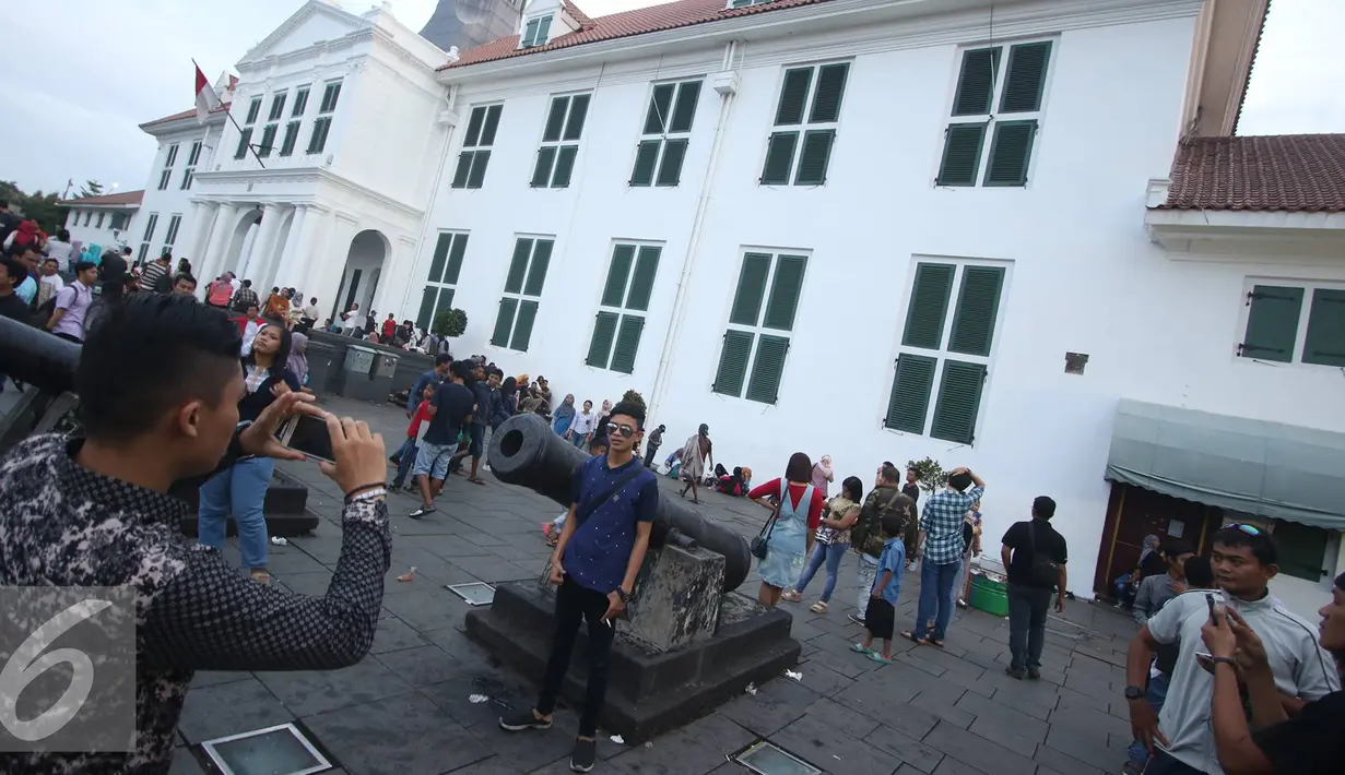 Pengunjung berfoto di depan meriam di kawasan wisata Kota Tua, Jakarta, Senin (12/12). Kota Tua masih menjadi salah satu destinasi wisata bagi warga Jakarta dan sekitarnya untuk menghabiskan waktu liburan. (Liputan6.com/Immanuel Antonius)